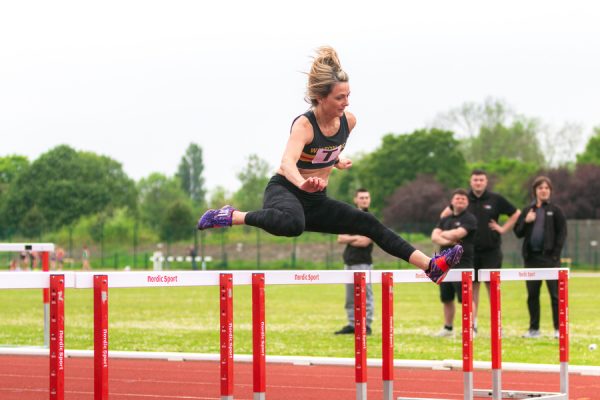 Lady jumping a hurdle on an athletics track