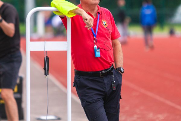 Man in red t-shirt standing next to an athletics track